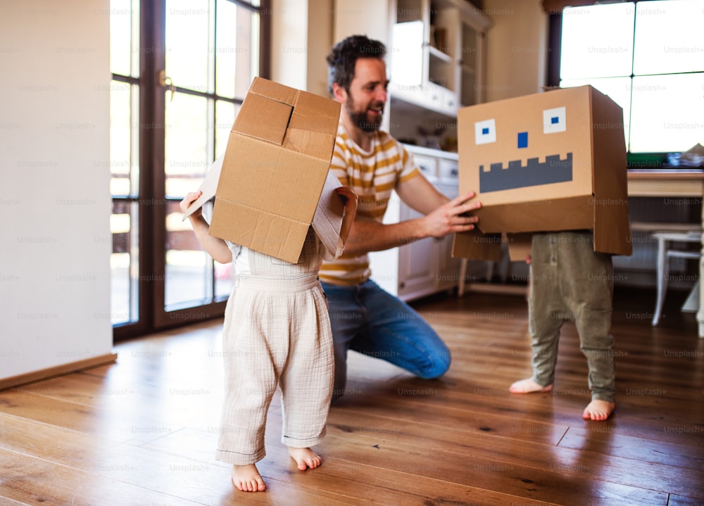 Duas crianças felizes com um pai e um monstro de papelão brincando dentro de casa.