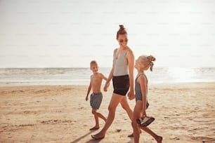 Smiling Mom and her two children holding hands together while walking along a sandy beach during summer vacation