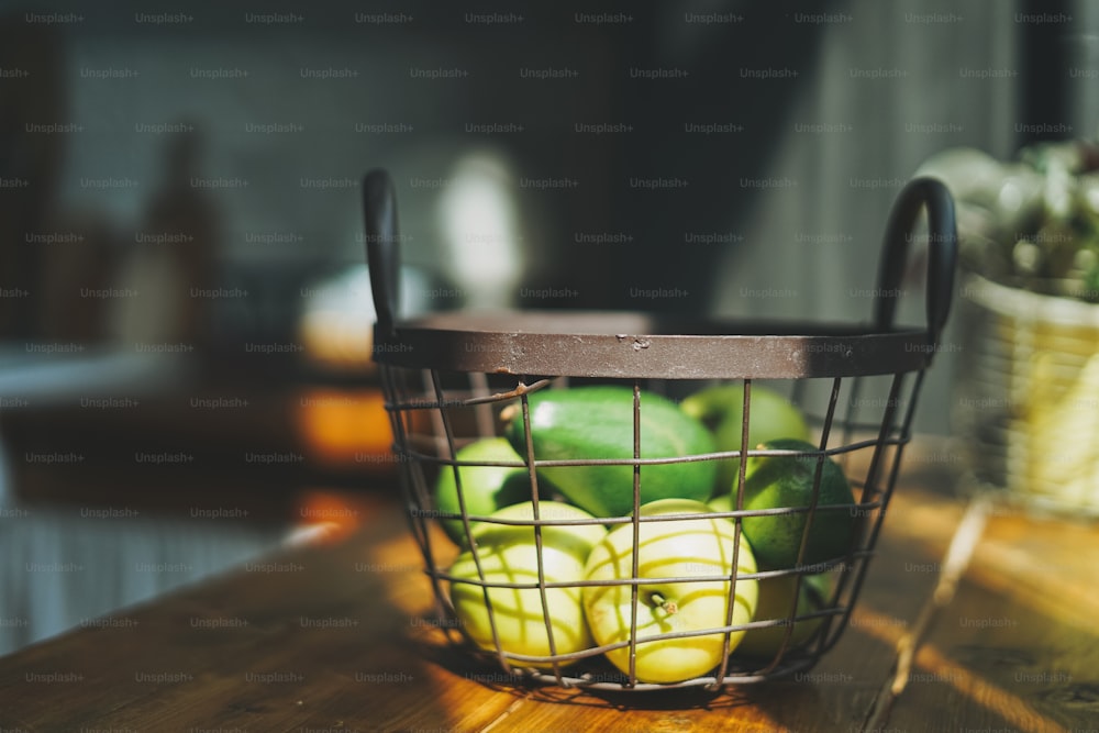 Reife rohe frische grüne Avocado und Äpfel im Metallkorb in der Küche, hartes Sonnenlicht