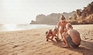 Mãe sorridente e seus dois filhos brincando na areia durante umas férias juntos na praia