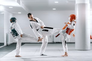 Garçons caucasiens sportifs s’entraînant au taekwondo dans un gymnase blanc. Entraîneur faisant une démonstration de coup de pied.