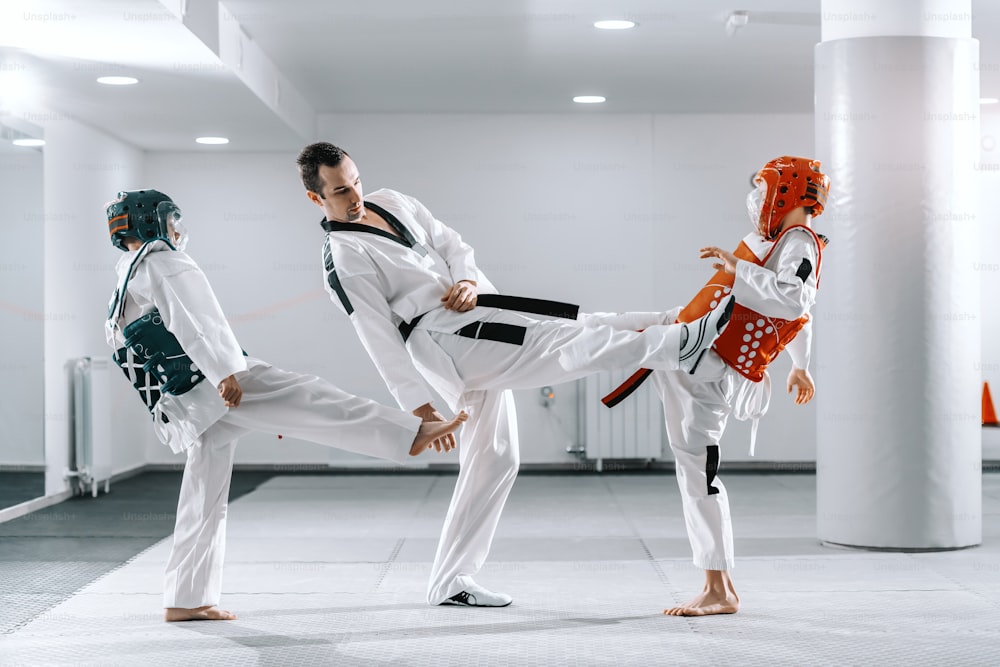 Ragazzi caucasici sportivi che si allenano con il taekwondo nella palestra bianca. Allenatore che dimostra il calcio.