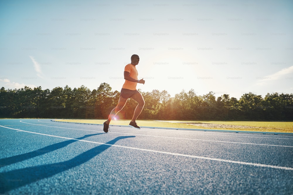 Giovane atleta maschio africano focalizzato in abbigliamento sportivo che corre lungo una pista da corsa in una giornata di sole