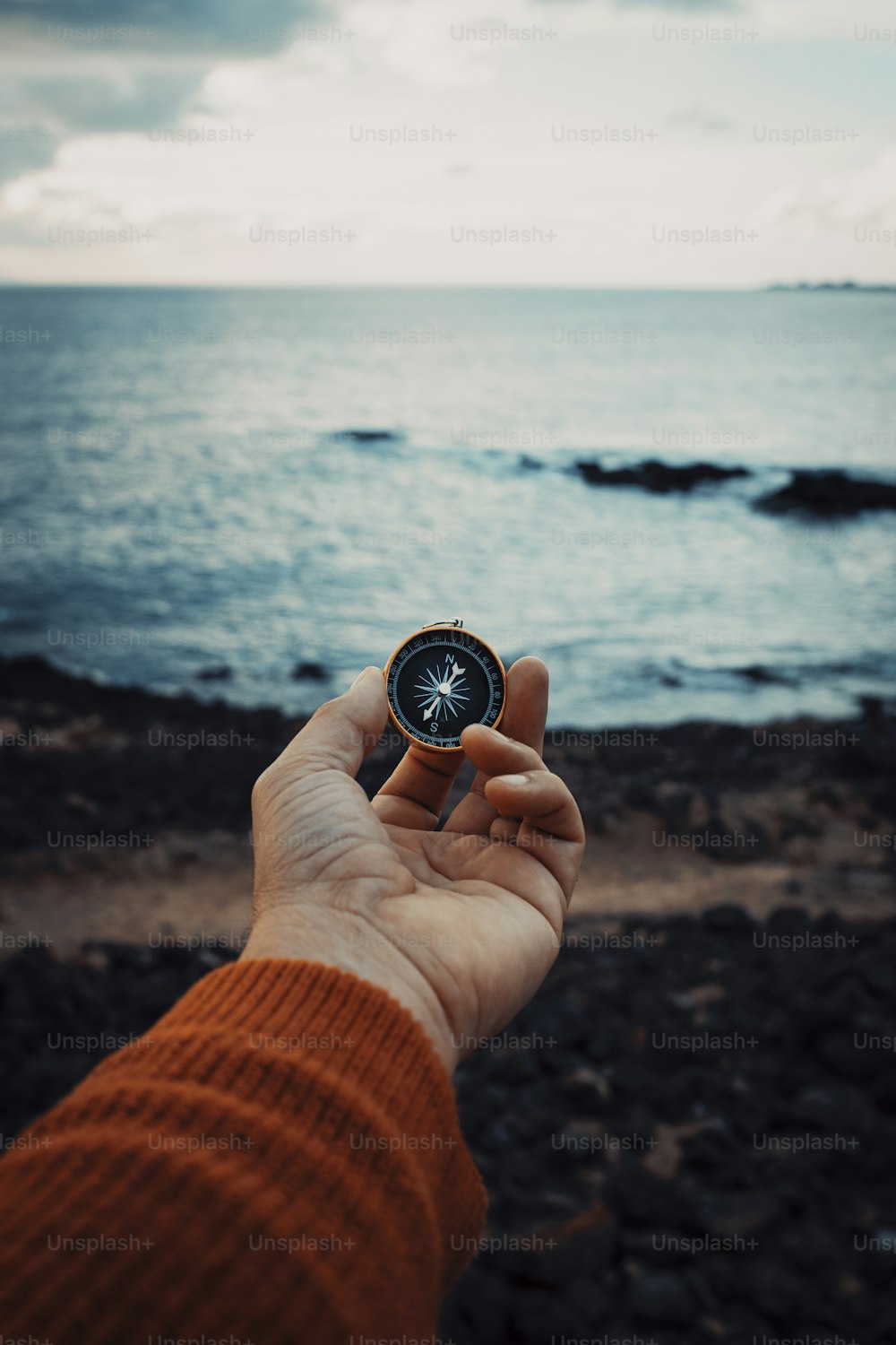 Pov of man hand holding navigational travel compass to find direction and next destination place. Concept of travel people and exploring. Beach and ocean with sky light in background