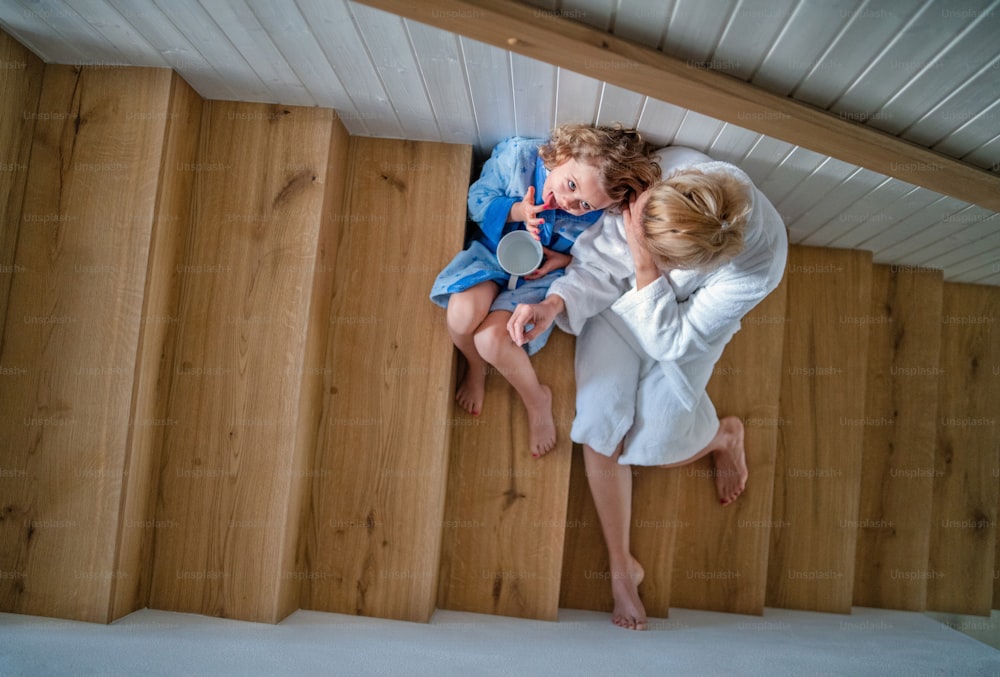 Eine Draufsicht auf ein kleines Mädchen mit Mutter drinnen zu Hause, morgens auf der Treppe sitzend.