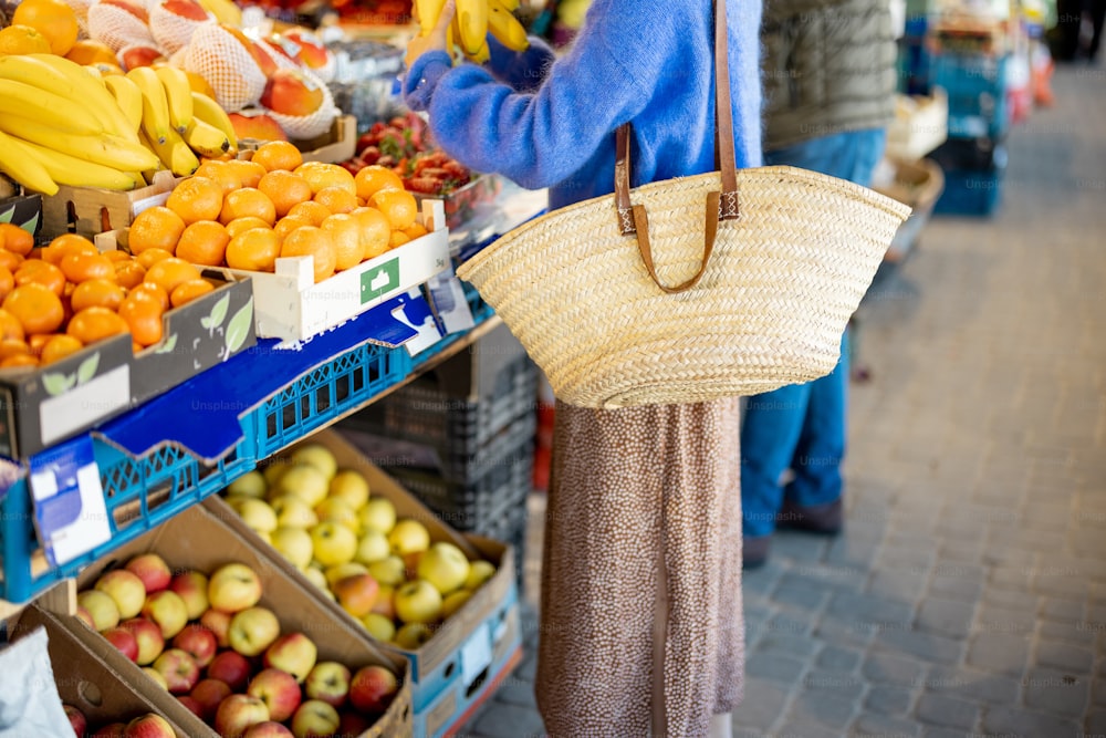 Mulher que compra frutas com saco de malha reutilizável no mercado local. Vista recortada sem rosto. Sustentabilidade e conceito de alimentos orgânicos locais