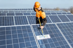 Limpiador profesional con ropa de trabajo protectora limpiando paneles solares con una turba. Concepto de servicio de limpieza de plantas de energía solar