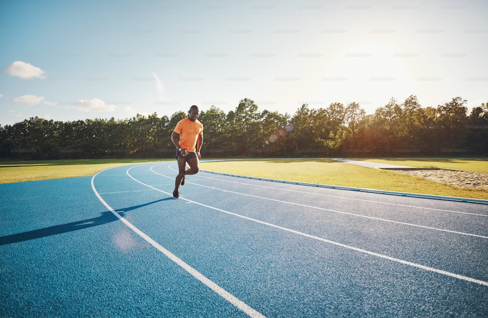 Fokussierter junger afrikanischer Athlet in Sportbekleidung, der an einem sonnigen Tag alleine über eine Laufstrecke sprintet