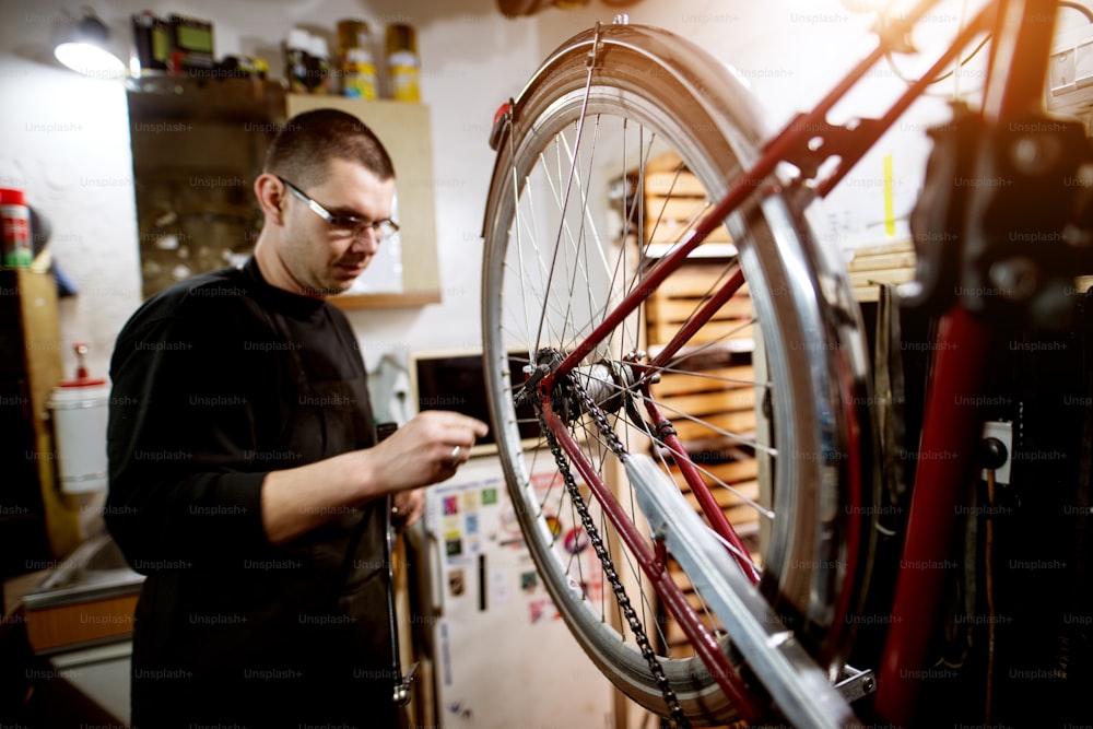 Young guy checking bicycle wheel balance in the garage.