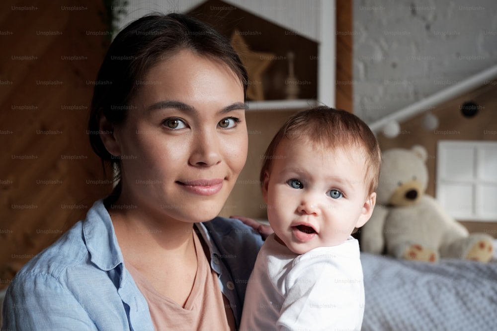 Retrato em close-up da bela mãe jovem que passa o tempo em casa segurando a filha bebê nos braços olhando para a câmera