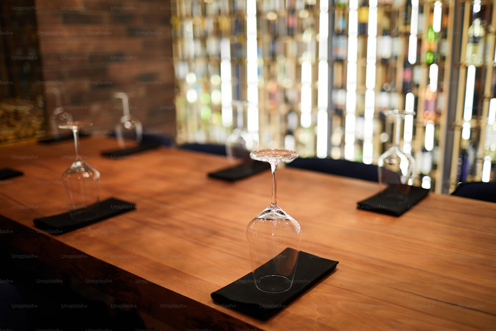 Wooden table in restaurant served with several wineglasses standing upside down on folded black napkins