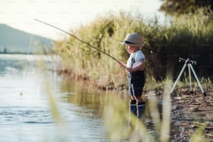 Um menino pequeno em pé à beira de um lago ao pôr do sol, pescando. Espaço de cópia. Espaço de cópia.