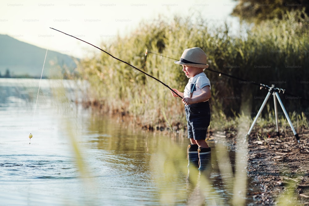 A small toddler boy standing by a lake at sunset, fishing. Copy space. Copy space.