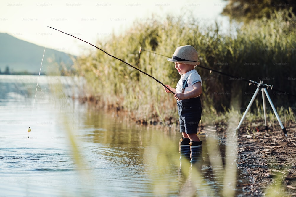 Un piccolo bambino in piedi vicino a un lago al tramonto, pescando. Copia spazio. Copia spazio.