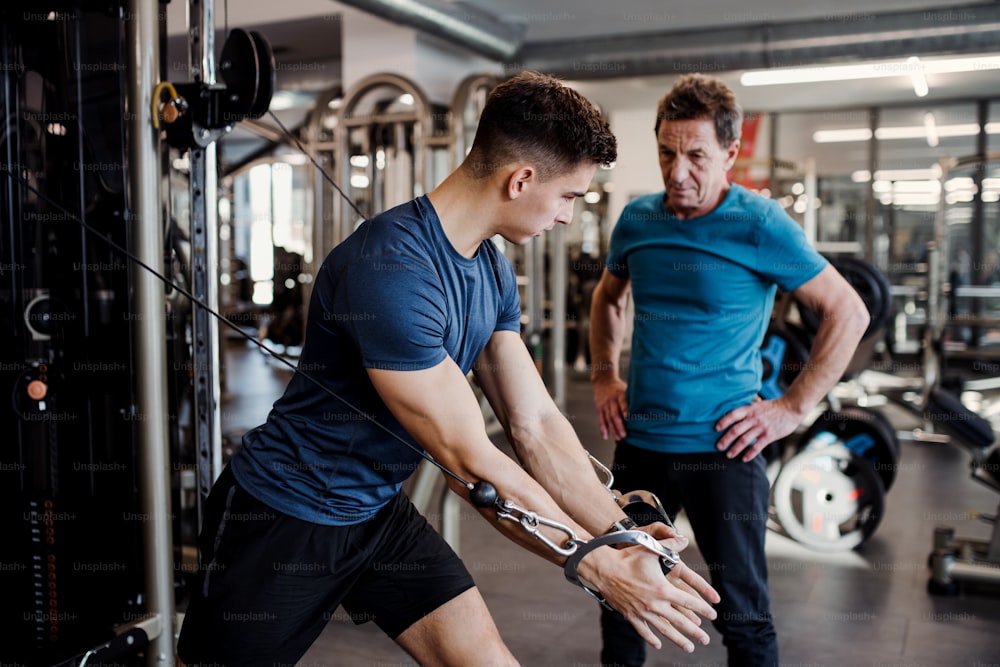 Um homem sênior com um treinador masculino jovem fazendo exercícios de força na academia.