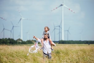 Reifer Vater mit kleiner Tochter, die auf dem Feld des Windparks spazieren geht und sie Huckepack fährt.