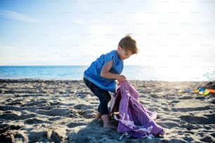 A portrait of happy small girl standing outdoors on sand beach, playing.
