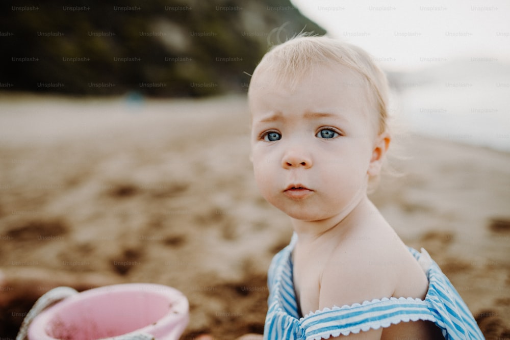 A close-up of small toddler girl on beach on summer holiday, playing. Copy space.