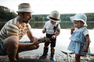 A mature father with small toddler children fishing by a river or a lake, holding a fish.