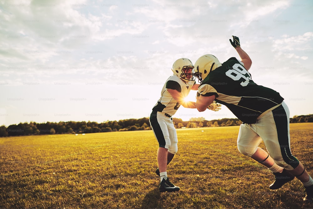Junge American-Football-Spieler machen Tackling Drills, während sie am Nachmittag gemeinsam draußen auf einem Rasenfeld üben