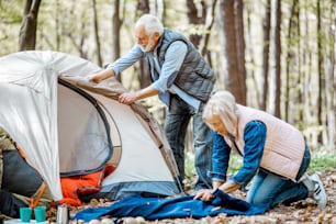 Seniorenpaar, das sich auf die Ruhe vorbereitet, ein Zelt und ein Plaid im Wald aufbaut