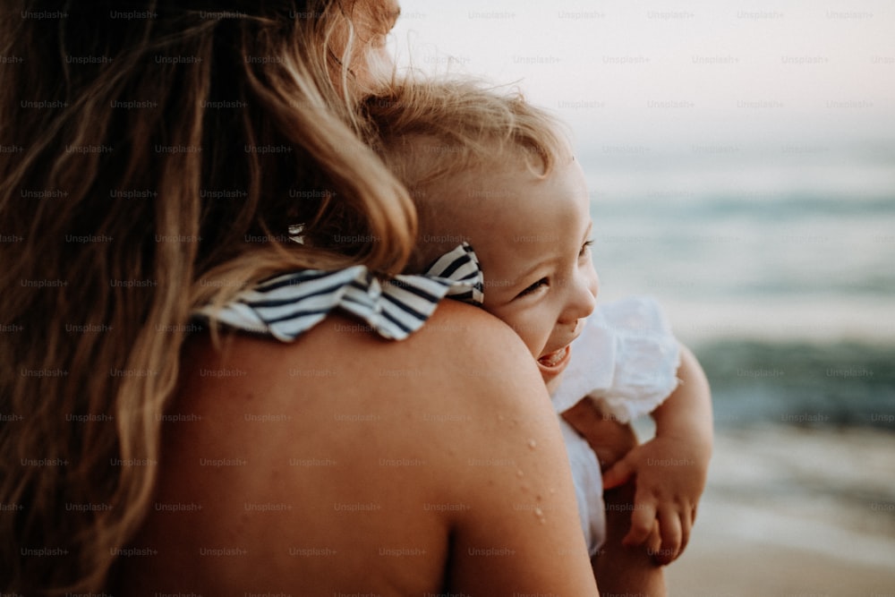 夏休みのビーチでよちよち歩きの女の子を持つ若い母親のクローズアップ。