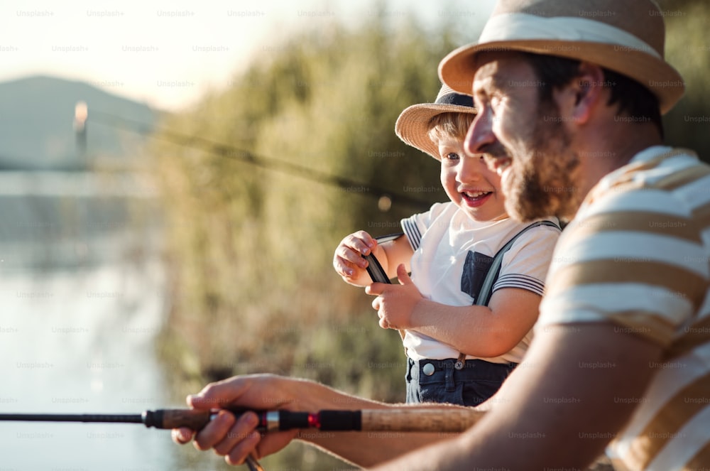 Un padre maturo con un figlio piccolo all'aperto che pesca in riva a un fiume o a un lago.