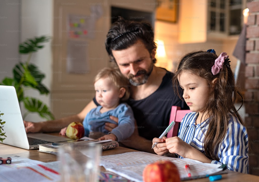 Padre maduro con hijas pequeñas en cocina, aprendizaje a distancia, oficina en casa y concepto de escolarización.