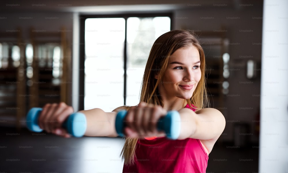 A portrait of a beautiful young girl or woman doing exercise with a dumbbells in a gym.