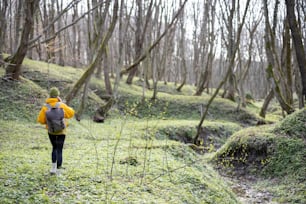 Young woman in hiking clothes and backpack staying and breathing fresh air in green spring forest. Enjoys and explore of tranquil nature. General plan.