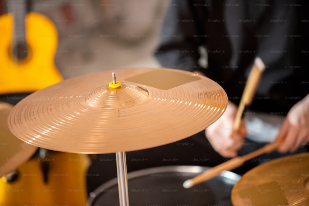 Rundes goldfarbenes Becken als Teil des Schlagzeugs auf dem Hintergrund eines zeitgenössischen Musikers im schwarzen Sweatshirt während der Probe