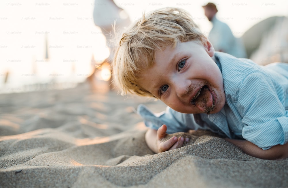 Un niño pequeño y alegre de pie en la playa en vacaciones de verano, divirtiéndose.