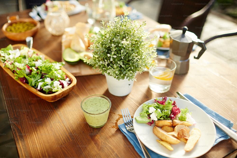 Copo de smoothie de legumes frescos, salada e batatas assadas no prato, limonada caseira e outros alimentos servidos na mesa