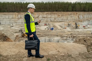 Young foreman with handbag and digital tablet walking along quarry