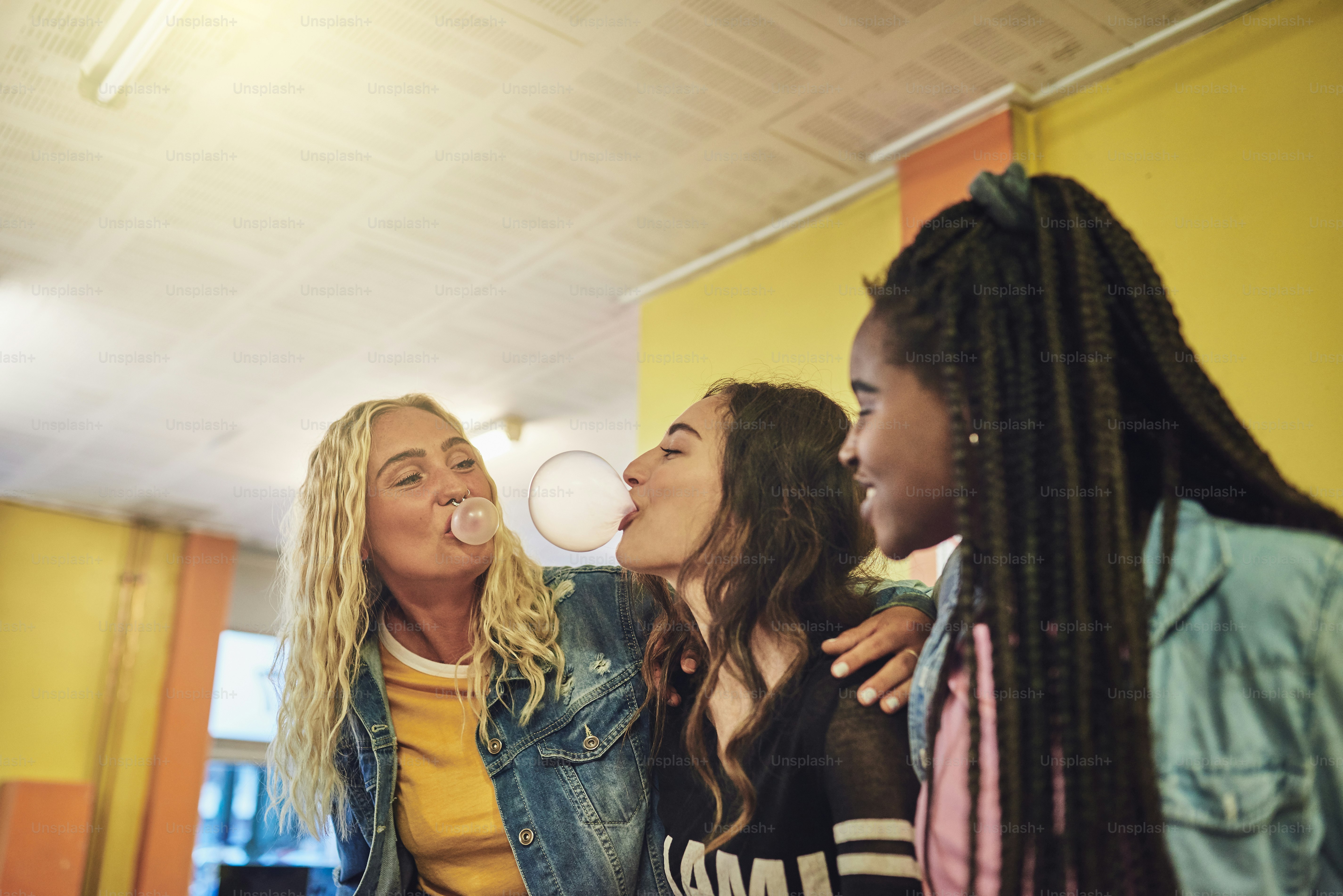 Groupe de jeunes copines traînant dans une laverie ensemble en riant et en soufflant des bulles avec du chewing-gum