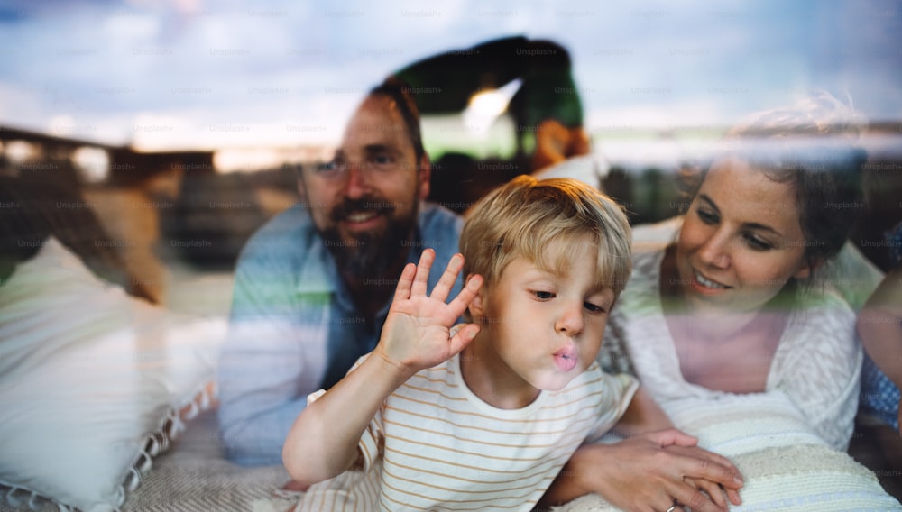 Portrait of small boy with parents by window, holiday in nature concept. Shot through glass.