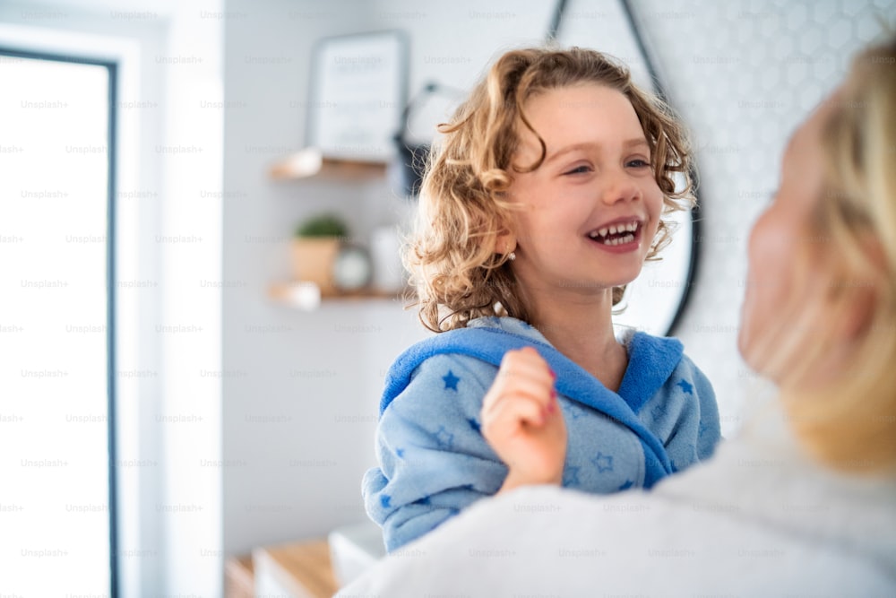 A cute small girl with unrecognizable mother in bathroom indoors at home, laughing.