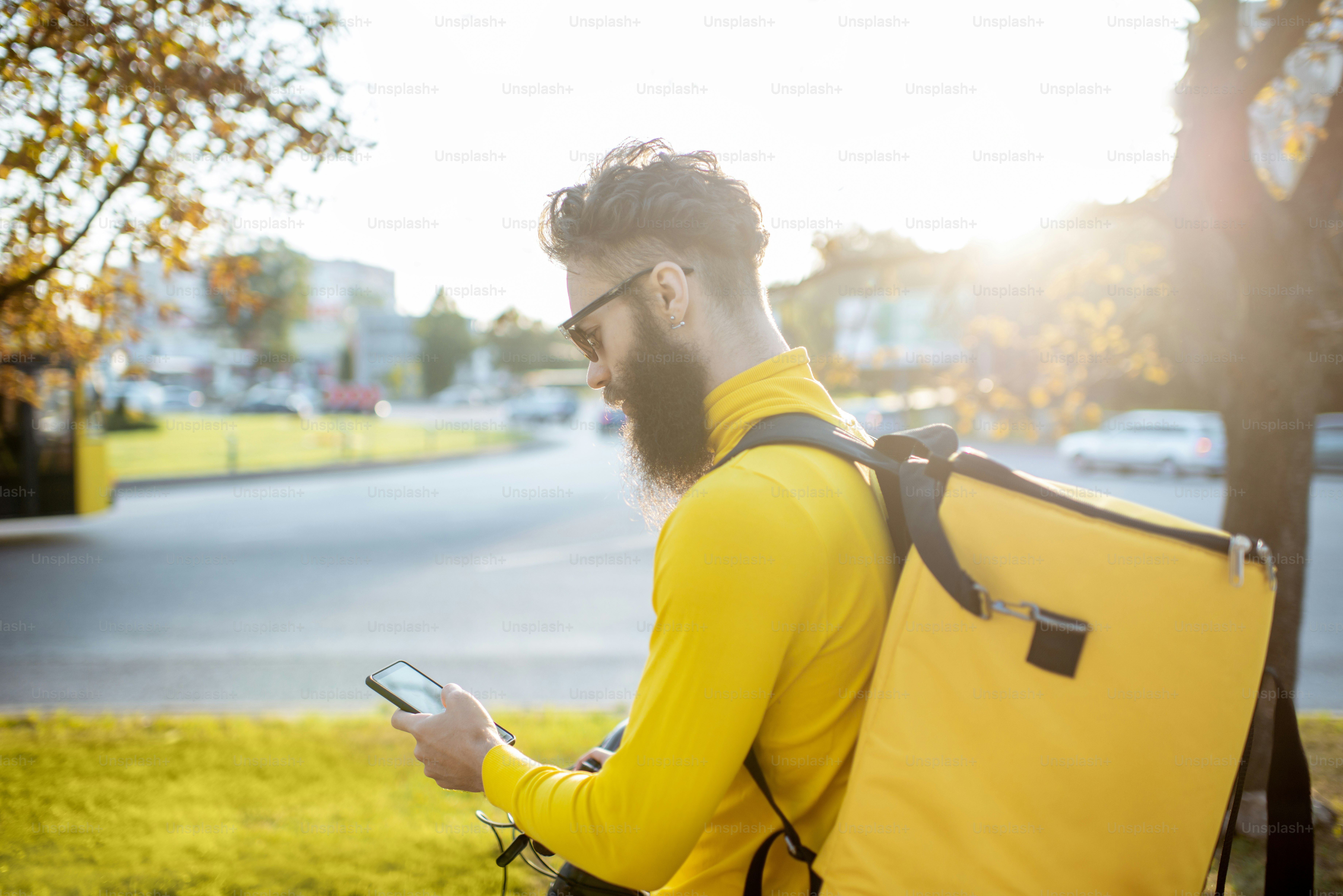Giovane corriere che consegna cibo su una bicicletta, controllando l'ordine con uno smartphone mentre si trova per strada in città. Concetto di servizio di consegna
