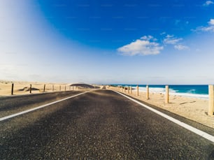 Strada lunga per il concetto di trasporto dell'automobile di viaggio con il deserto e la spiaggia sul lato - acqua di mare e cielo limpido blu bello sullo sfondo - effetto di movimento