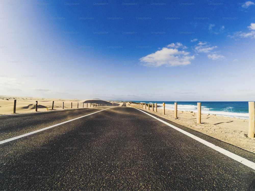 Camino largo para el concepto de transporte de automóviles de viaje con desierto y playa en el costado - agua de mar y cielo hermoso claro azul en el fondo - efecto de movimiento
