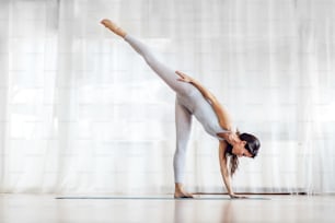 Atractiva morena joven en posición de yoga de media luna. Interior del estudio de yoga.