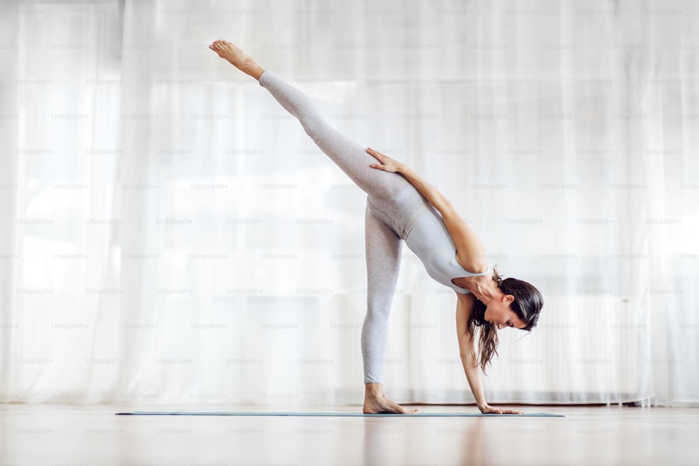 Attraente giovane bruna in posizione yoga a mezza luna. Interno dello studio di yoga.