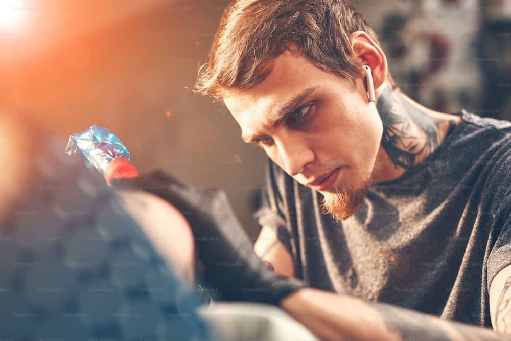 A young guy, beats a tattoo on the hand of the girl in a tattoo parlor, rotary tattoo machine, black ink, lens flare