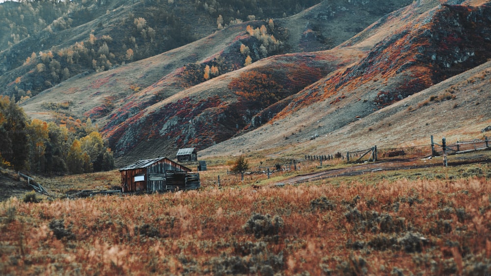 Increíble paisaje montañoso con una conejera de madera abandonada y el prado en primer plano y la cresta de las colinas y con pastos y establos al fondo; principios de otoño en las montañas de Altai