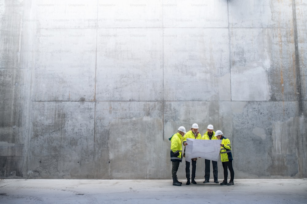 Un groupe d’ingénieurs debout contre un mur de béton sur un chantier de construction, tenant des plans. Espace de copie.