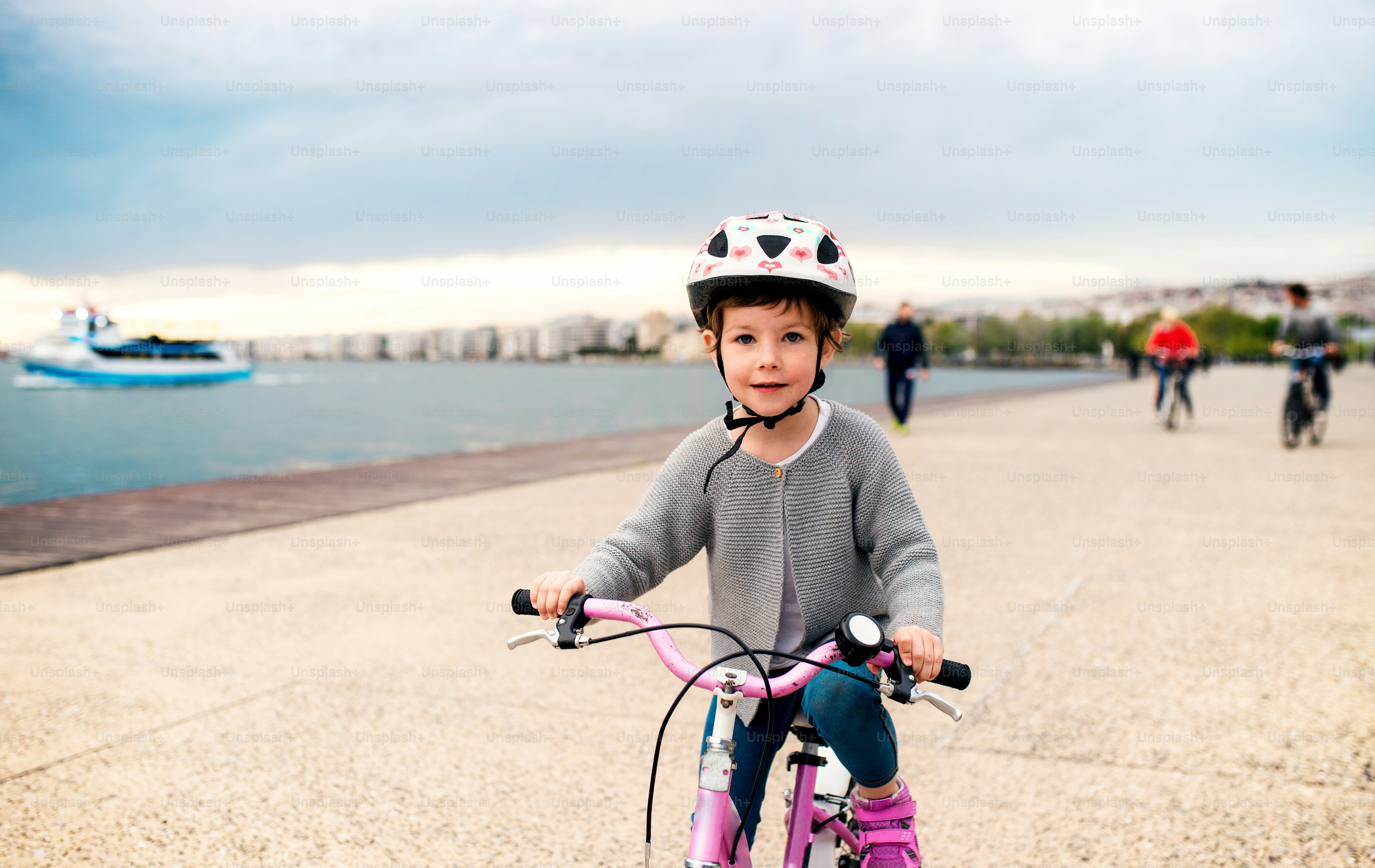 Una niña pequeña con casco y bicicleta pedaleando al aire libre en la playa.