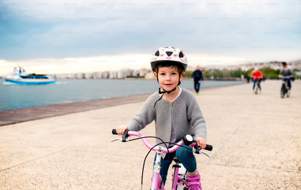 A small girl with helmet and bicycle cycling outdoors on beach.