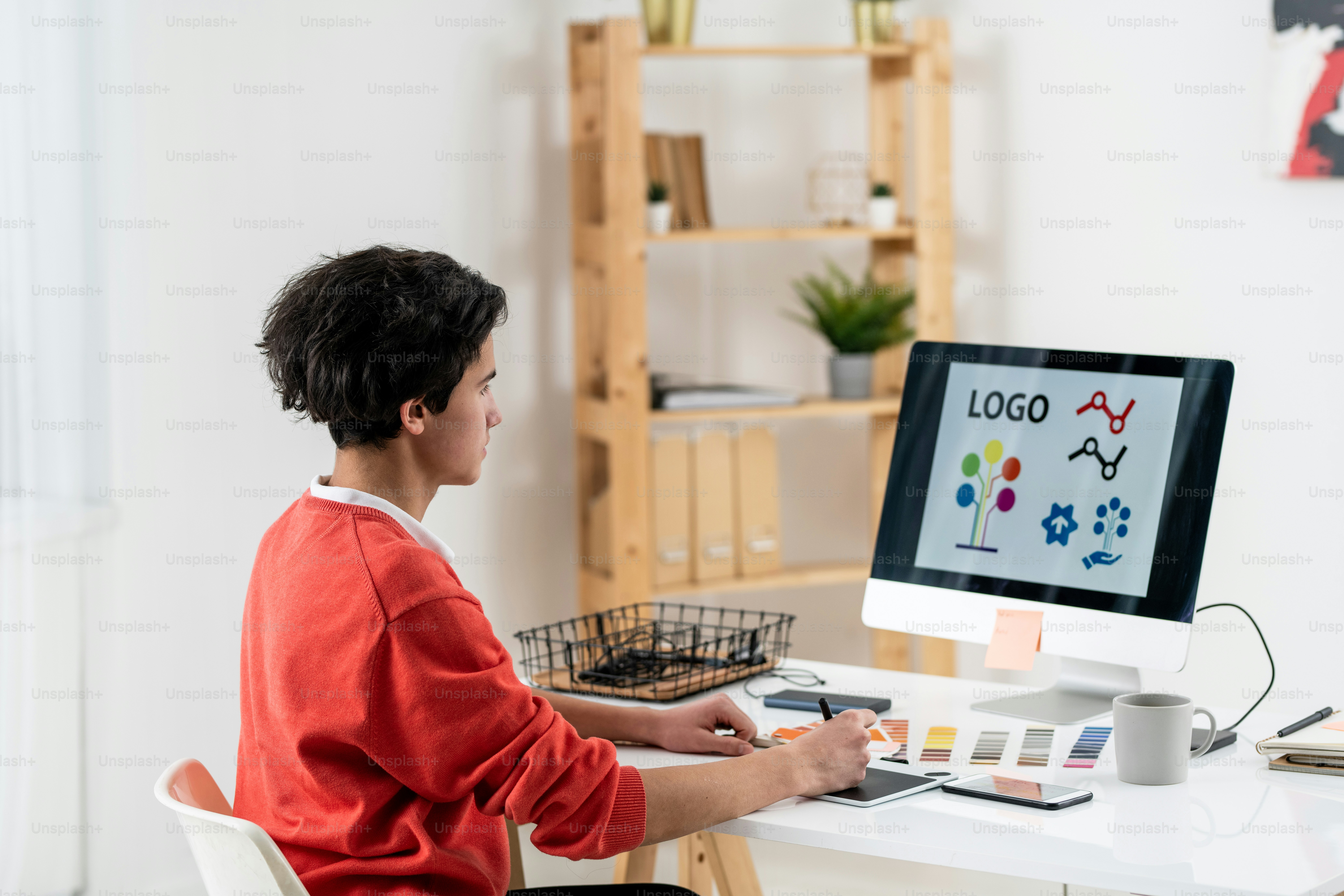 Zeitgenössischer Webdesigner mit Grafiktablett, der ein neues Logo zeichnet, während er am Schreibtisch vor dem Computerbildschirm sitzt