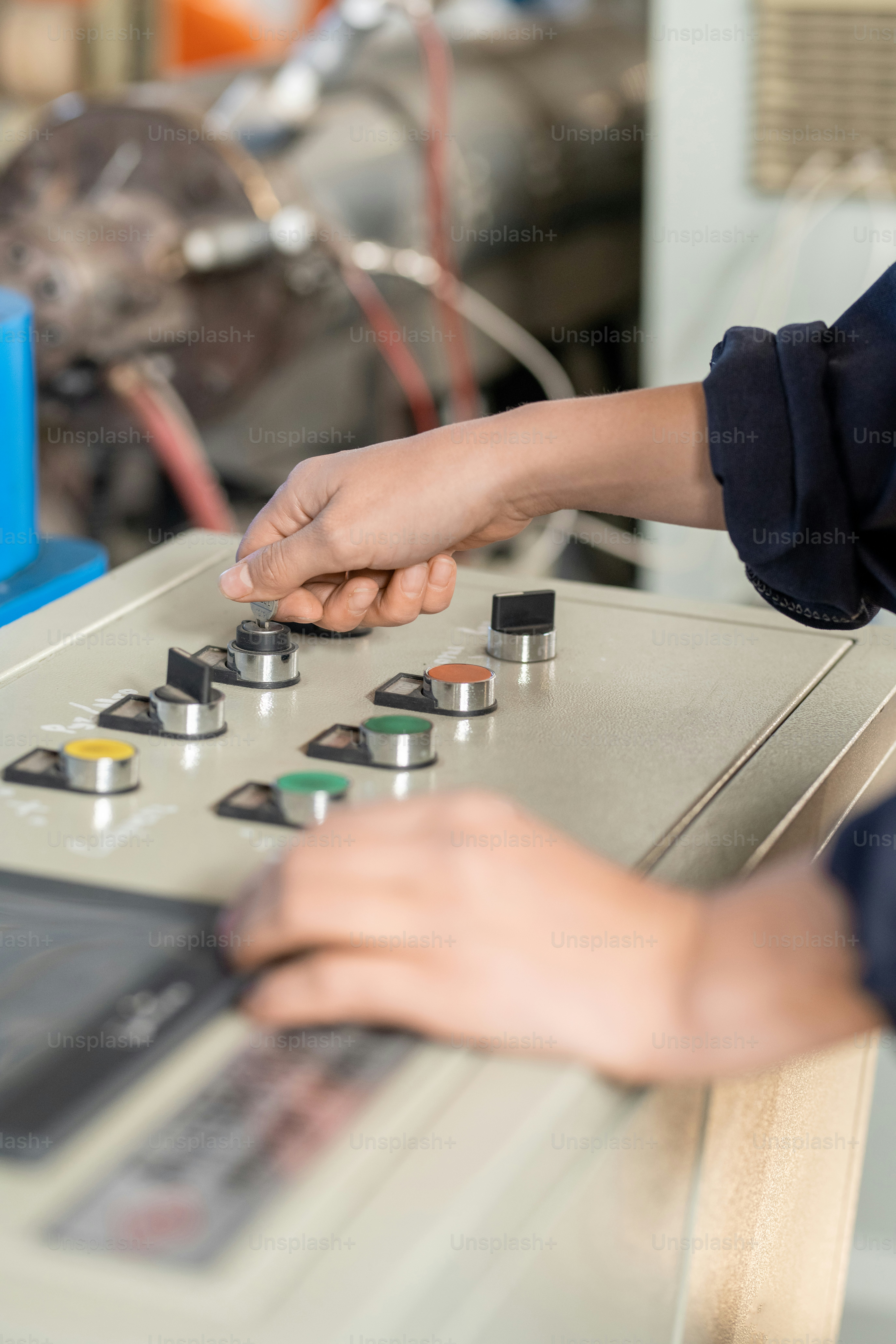 Hand of young female worker in overalls standing in front of control panel and turning knobs while preparing industrial machine for work