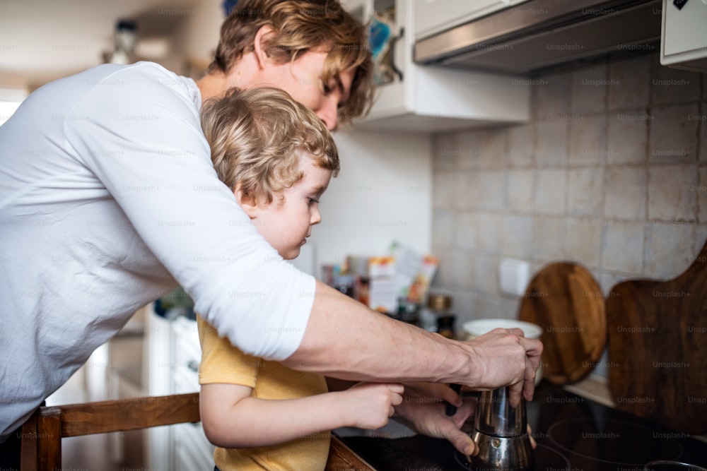 Ein junger Vater mit einem kleinen Sohn, der Zeit in einer Küche zu Hause verbringt.